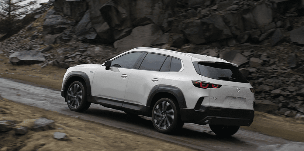 Vue 3/4 arrière du Mazda CX-50 hybride 2025 roulant sur un chemin.